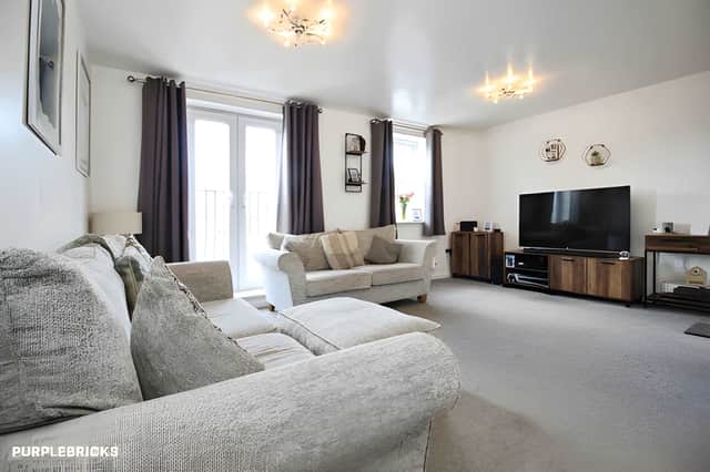 The first-floor lounge features neutral décor, carpeted flooring and a Juliet balcony window that brings natural light into the living space