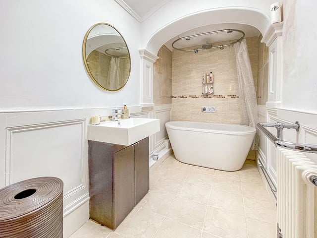 A modern bathroom includes a washbasin with vanity unit and a deep bath tub with shower over.