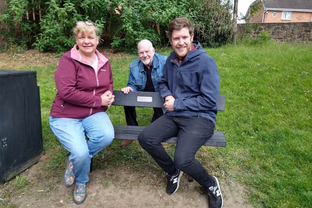 Emma and Ben Crowley sitting on the commemorative bench with Niall Walker (kneeling)
