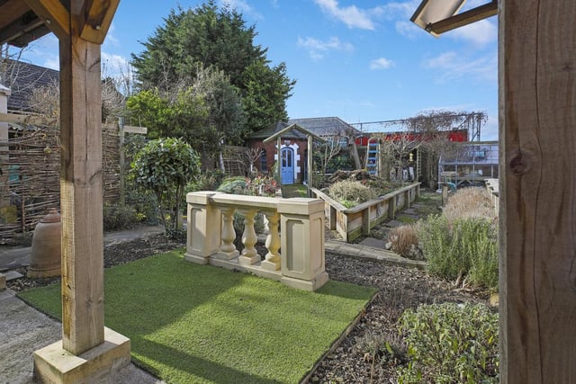 A lawned and low maintenance rear garden with seating areas, planters, vegetable plots, a summer house and a water feature.