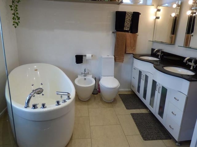 This bathroom has a free standing jacuzzi bath, a double walk-in shower and twin wash basins within a vanity unit setting.