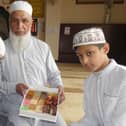 Mosque leader Haji Liaquat Ali with his two grandsons, Kaif Ali and Kareem Ali, holding boxes of traditional Indian 'Methai' sweets inside the main prayer hall of their local Anwaar-E-Madina Jamia Mosque on the day of Eid-Ul-Fitr
