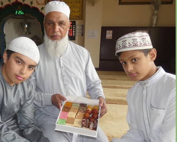 Mosque leader Haji Liaquat Ali with his two grandsons, Kaif Ali and Kareem Ali, holding boxes of traditional Indian 'Methai' sweets inside the main prayer hall of their local Anwaar-E-Madina Jamia Mosque on the day of Eid-Ul-Fitr