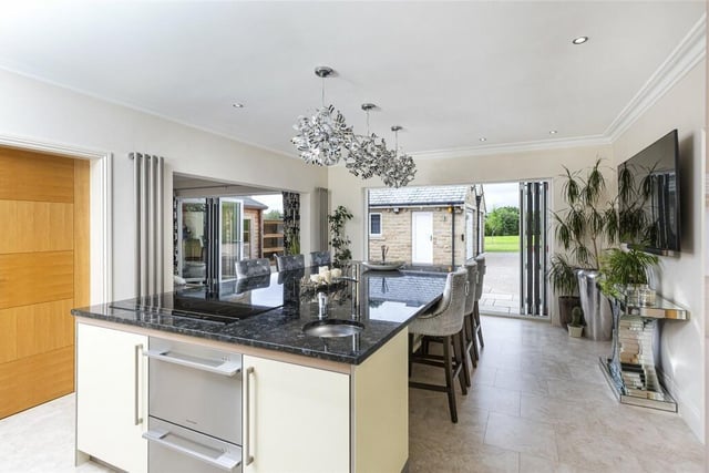 A large granite island has seating in the kitchen with bi-fold doors to outside.