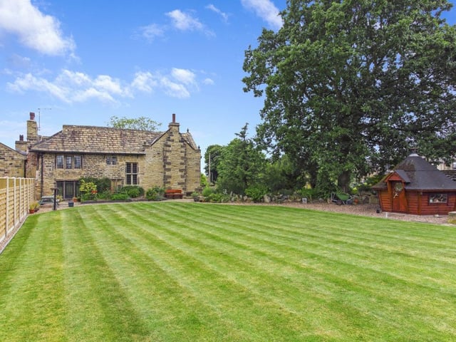 A patio area, lengthy lawn, and barbecue hut feature in the private rear garden.