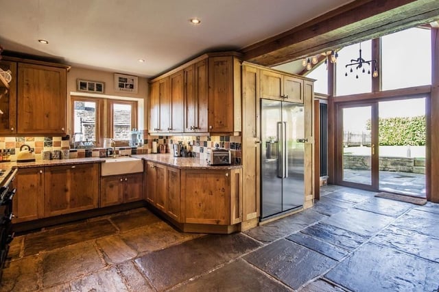 A rustic style kitchen with doors leading outside has solid wood units with granite worktops, a Belfast sink, a range style cooker and stone flooring.