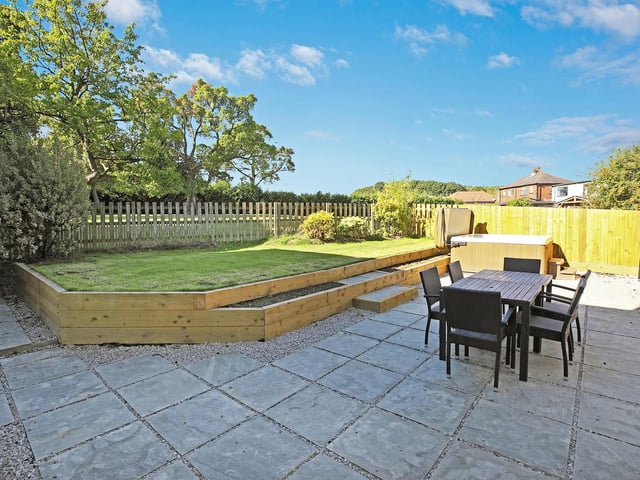 A large York stone patio with steps up to a lawned area.