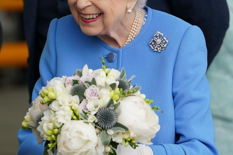 Queen Elizabeth II receives flowers as she meets employees.