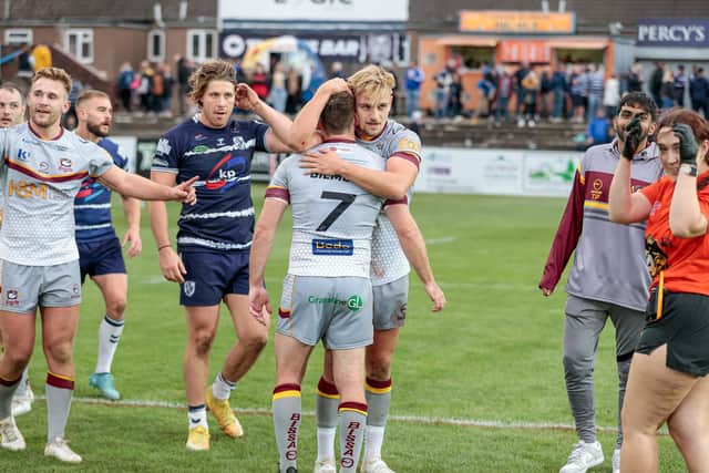 Tom Gilmore, wearing number 7, receives a hug from Luke Hooley following the Bulldogs' 32-28 triumph at Featherstone Rovers which has taken the club to within 80 minutes of a place in Super League.