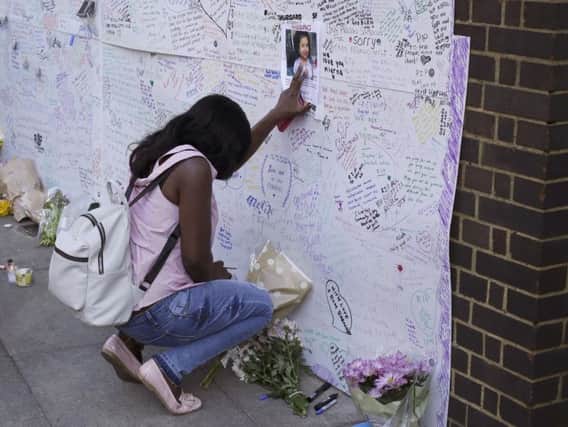 A woman touches a missing poster for 12-year-old Jessica Urbano on a tribute wall after laying flowers on the side of Latymer Community Church next to the fire-gutted Grenfell Tower in London.